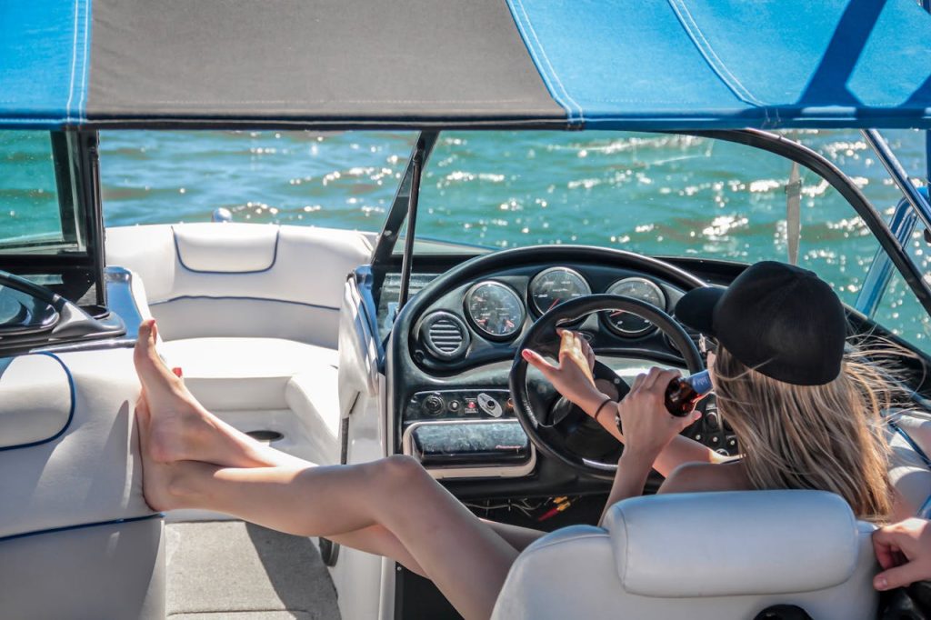 woman-wearing-black-cap-holding-bottle-on-white-speedboat-during-daytime-209978 A woman enjoys a sunny day on a luxury boat, relaxing with a beverage.