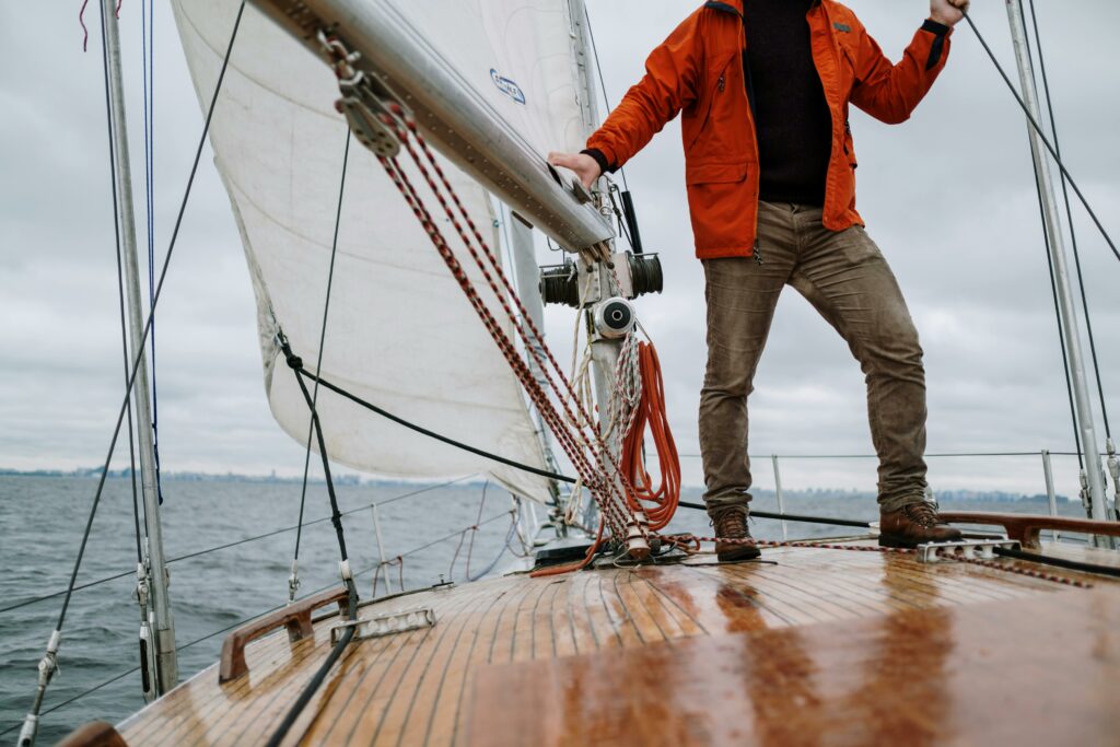 pexels-photo-5416470-5416470 Man standing on a sailboat enjoying the journey with a vast horizon in the background.